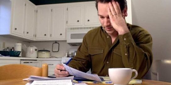 Tips to Catch Up on Bills When Falling Behind Man Stressed at Table Facing Bills