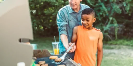 During a summer cookout, a man shows a boy how to grill hamburgers.